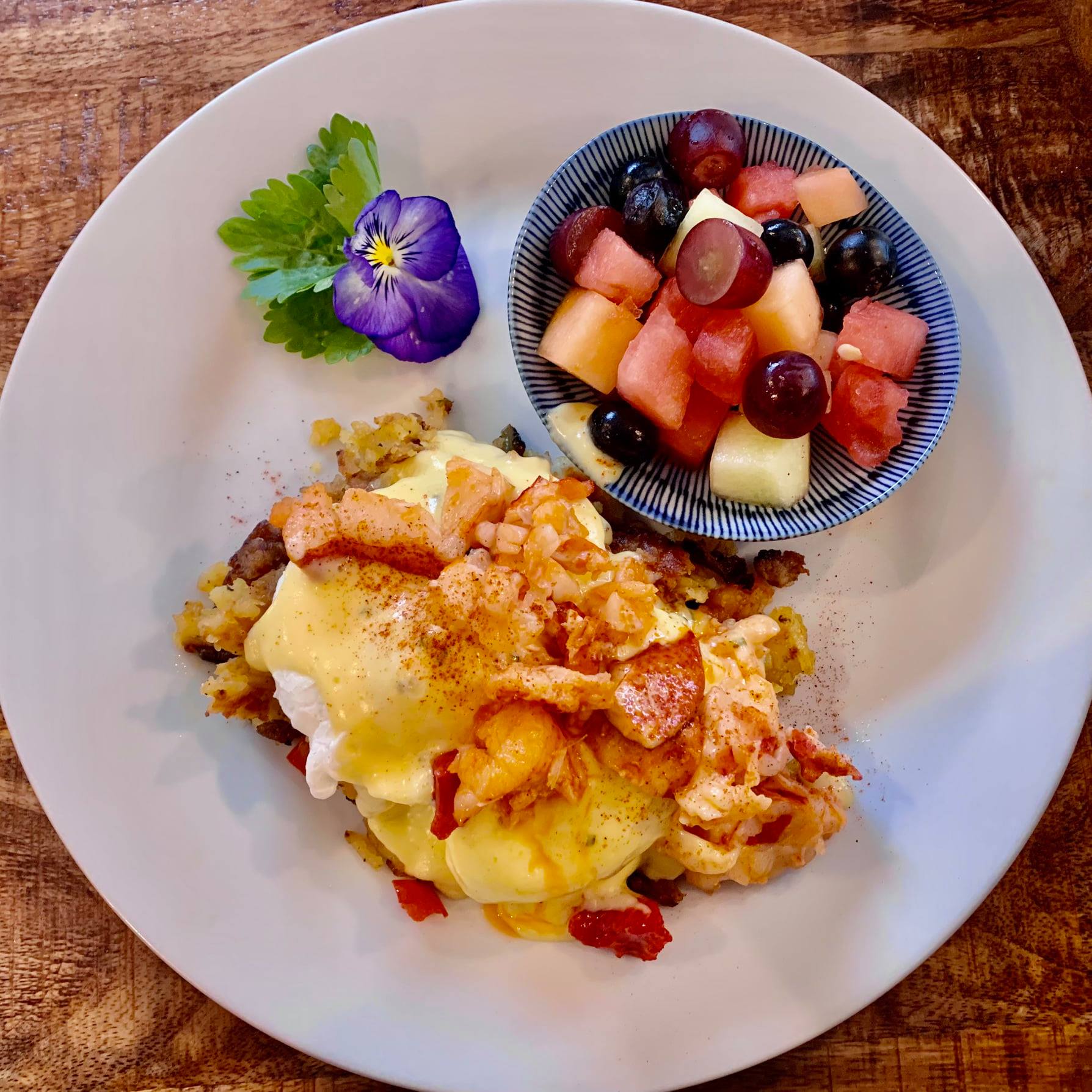 Lobster & Sausage Hash Benedict with zesty Hollandaise served with fresh lime dressed fruit bowl.